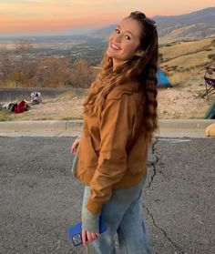 a girl with long hair holding a skateboard in her hand and looking up at the sky