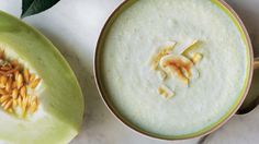 a bowl filled with soup next to a sliced melon on top of a table