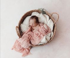 a newborn baby is sleeping in a wicker basket on a white background with pink blanket