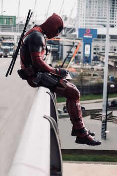 a man dressed as deadpool sitting on a rail