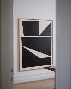 an abstract black and white painting hangs in the corner of a room next to a table