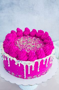 a pink cake with white icing and sprinkles on the top is sitting on a plate