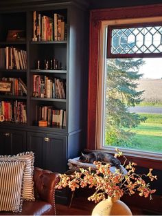 a living room filled with furniture and a large window covered in bookshelves next to a brown leather couch