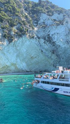 a large boat in the water with people on it near a rocky cliff and beach