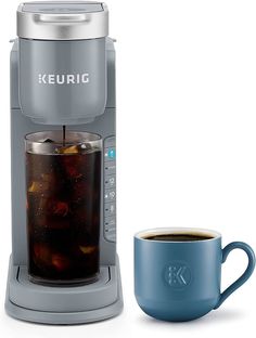 a keurig coffee maker next to a cup of tea and a blue mug