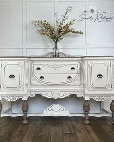 a white dresser with flowers on top of it in front of a wooden floor and wall