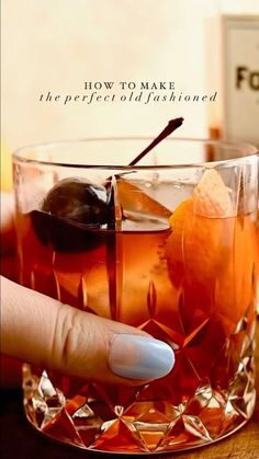 a hand holding a drink in front of a glass filled with ice and orange peels