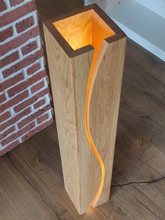 a wooden floor lamp with an orange light shining in it's center and on its side