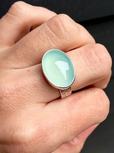 "A beautiful bright aqua blue oval chalcedony. This chalcedony is AAA quality and 100% natural. The stone has been set in sterling silver and a sterling silver bezel. The ring band is handmade from a sterling silver band with a unique pattern and is about 1/4\" wide or 6mm wide. Please note the width and thickness of the ring band and adjust your ring size as needed! The ring's total height is just over a 1/4\" and it is 13mm x 18mm in size. This stone is a light blue but certain light can bring Turquoise Oval Moonstone Ring For Anniversary, Oval Chrysoprase Opal Ring For Gift, Oval Turquoise Moonstone Ring, Turquoise Chalcedony Gemstone Rings, Aqua Chalcedony Ring, Spring Fashion Chic, Silver Jewlery, Christian Bracelets, Chalcedony Stone