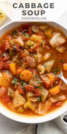 a white bowl filled with vegetable cabbage soup on top of a table next to bread