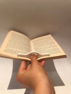 a hand holding an open book in front of a white wall with shadows on it