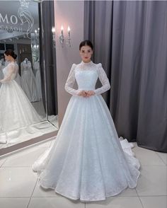 a woman standing in front of a mirror wearing a white wedding dress with long sleeves