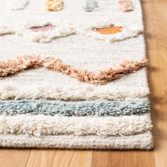 a white rug with multicolored fringes on top of a wooden floor next to a wood floor