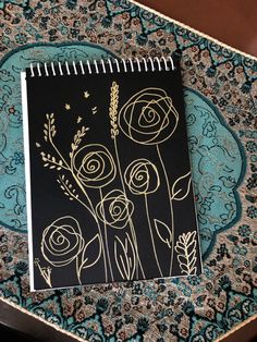 a black notebook with gold foil flowers on it sitting on top of a blue doily