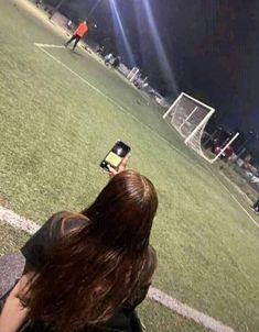 a woman sitting on top of a soccer field holding a cell phone in her hand