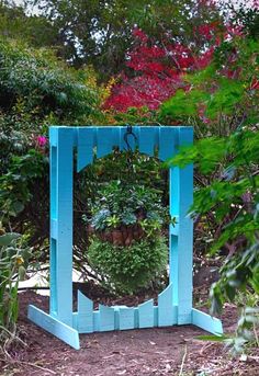 a potted plant hanging from a blue frame in the middle of some bushes and trees