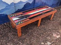 a wooden bench with colorful skis painted on the top and bottom sitting in front of a wall