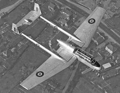 an old airplane flying in the sky over some buildings and grass with other planes around it