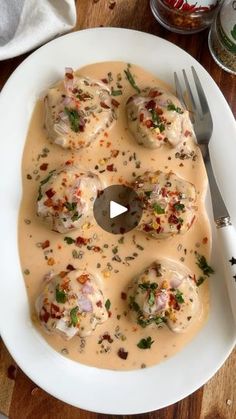 a white plate topped with dumplings covered in gravy next to a fork