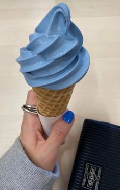 a person holding an ice cream cone with blue icing on it's top