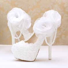 a pair of white high heeled shoes with flowers on the side and pearls around the heels