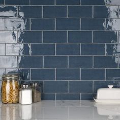 a blue brick wall in a kitchen with white counter tops and jars on the counter