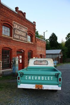 an old chevrolet truck is parked in front of a brick building that has a sign on it