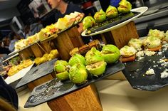 several trays filled with different types of food on wooden stands at a buffet table