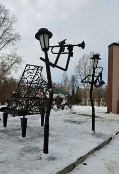 a park bench sitting next to two street lamps on top of snow covered ground with buildings in the background