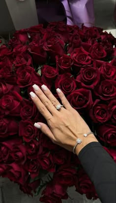 a woman's hand with white manicures and ring on top of a bouquet of red roses