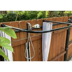 an outdoor shower is attached to the side of a wooden fence with metal bars and hoses