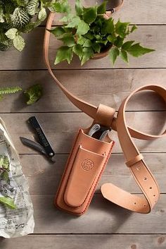 a brown leather case sitting on top of a wooden table next to scissors and plants