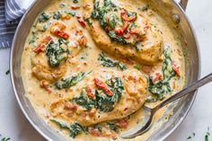 a pan filled with chicken and spinach on top of a white countertop next to silver spoons