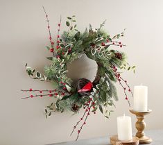 a christmas wreath with red berries, pine cones and a cardinal sits on a table next to two candles