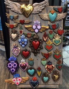 an assortment of heart shaped brooches are displayed on a wooden board with angel wings