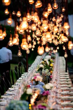 a long table with many lights hanging from it's ceiling and flowers on the table