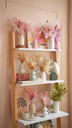 a shelf with vases and flowers on it in a room that has pink walls