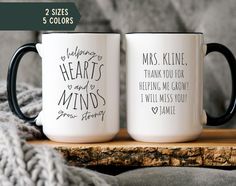 two coffee mugs sitting on top of a wooden table next to a gray blanket