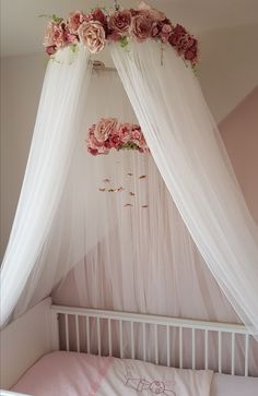 a canopy bed with pink flowers hanging from it's sides and white netting over the top