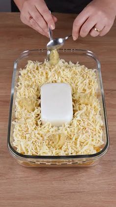 someone is spreading cheese on top of rice in a glass dish with a spoon to dip into it