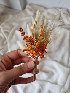 a person is holding some dried flowers on a bed with white sheets and blankets in the background