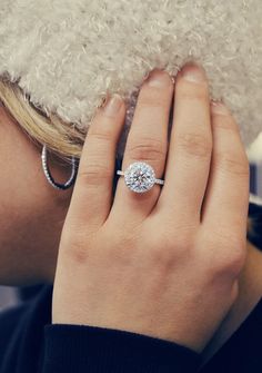 a woman wearing a diamond engagement ring on her left hand, with a white fur hat in the background