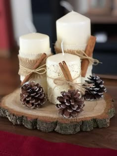 two white candles with cinnamon sticks and pine cones are on a wooden table next to other decorations