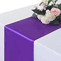 a purple and white table runner with flowers on it's end, along with greenery