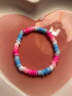 a pink, blue and white bracelet sitting on top of a heart shaped bowl