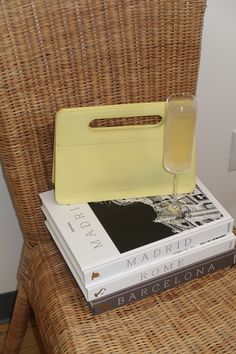 a stack of books sitting on top of a wicker chair next to a yellow purse