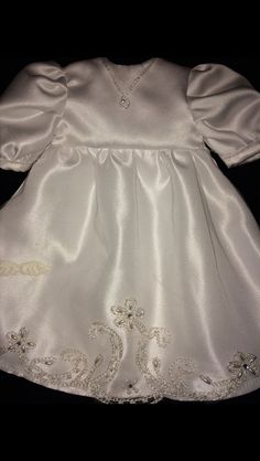 a white dress that is sitting on top of a black surface with an embroidered design