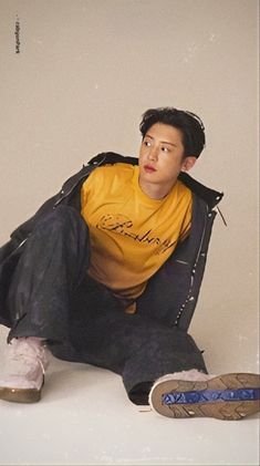 a young man sitting on the ground with his foot up in front of him, wearing a yellow shirt and black pants