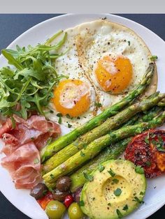 a white plate topped with asparagus, eggs and other food on top of it