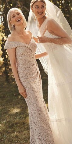 two women standing next to each other in front of trees and one wearing a wedding dress